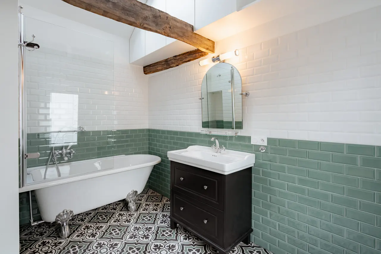 Salle de bains : baignoire sur pieds, carreaux de ciment, faïence verte.