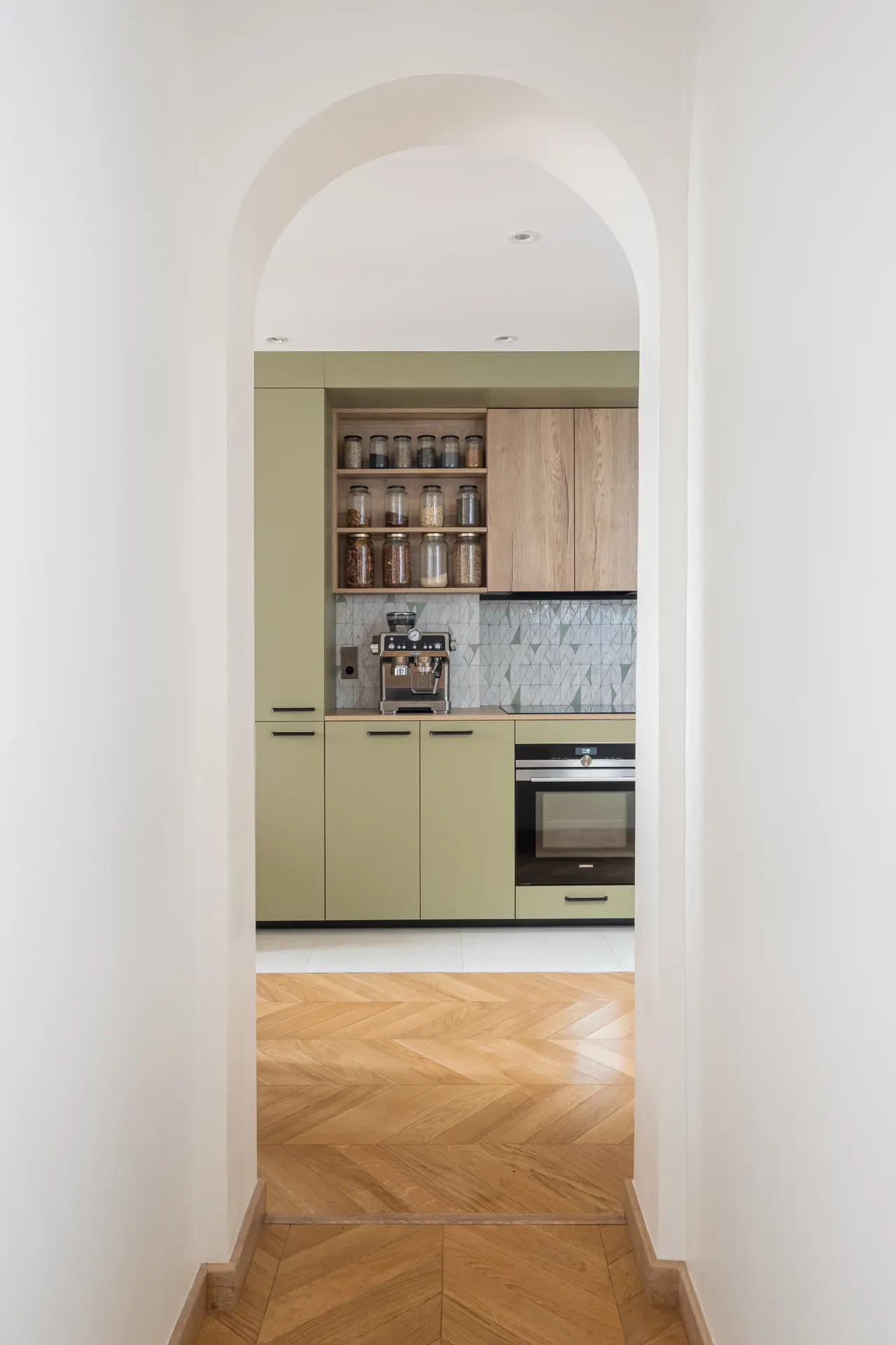 Une cuisine vert sauge vue à travers une arche.